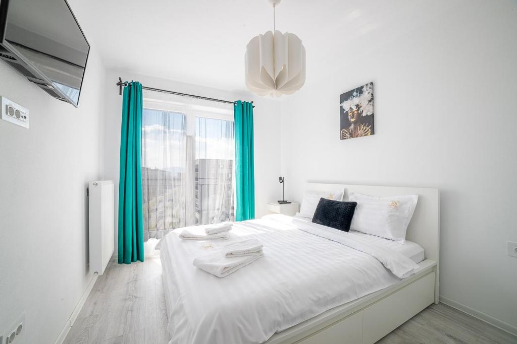 a white bedroom with a large bed with blue curtains at Modern Coresi Studio - Free Private Parking by MM Host in Braşov