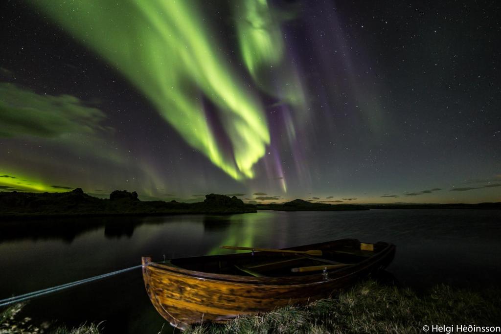 an old boat sitting in the water under the aurora at Dimmuborgir Guesthouse in Myvatn