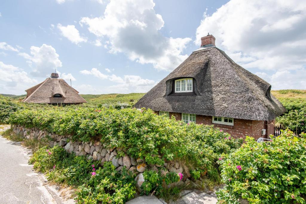 a house with a thatched roof and a stone wall at Haus Südkap in Hörnum