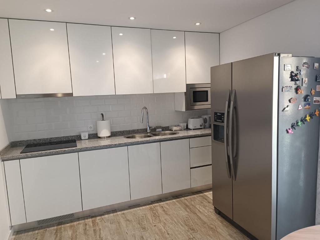 eine Küche mit weißen Schränken und einem Edelstahlkühlschrank in der Unterkunft Cachinnans Hostel & Apartments in Vila do Conde
