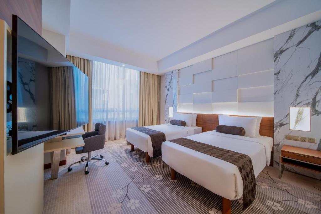 A twin room photographed from the television side, with a bright curtained window.
