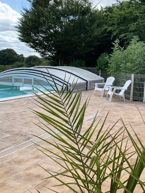 a patio with two white chairs and a swimming pool at Gite de Groupe Aux Instants Partagés in Fontenay-sur-Vègre