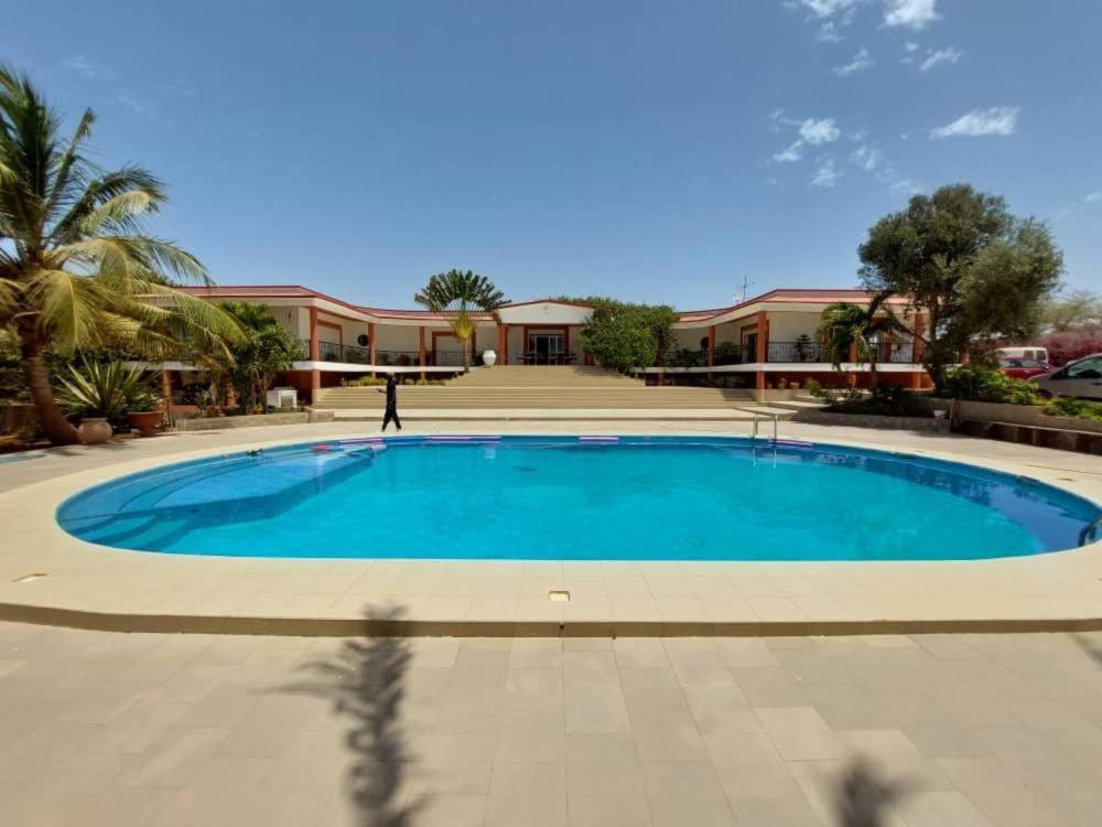 a large blue swimming pool in front of a building at Residence le belier in Mbirdiamm