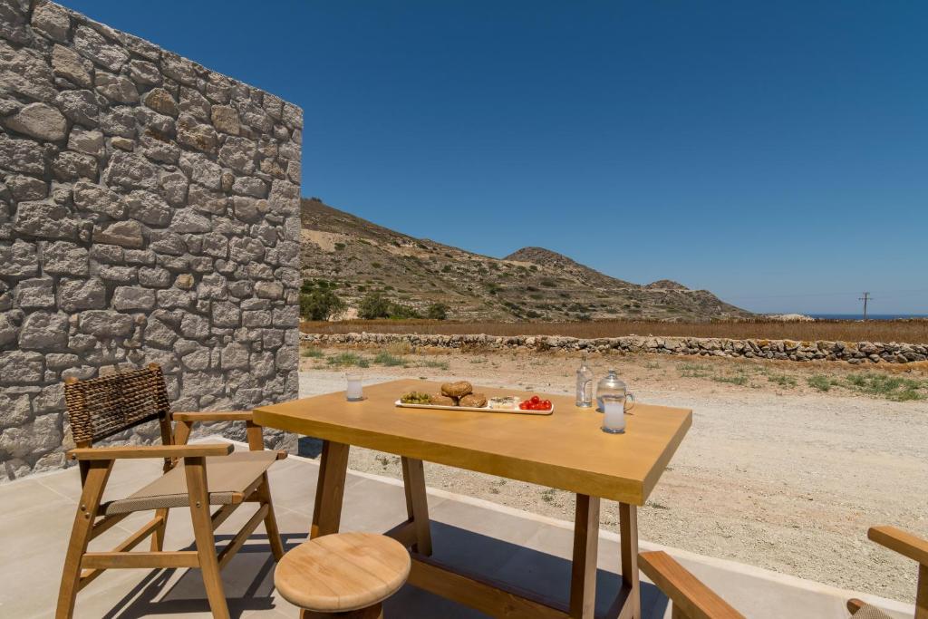 a wooden table and chairs in front of a stone wall at Katoikia Milos Slow Living Homes in Mandrakia