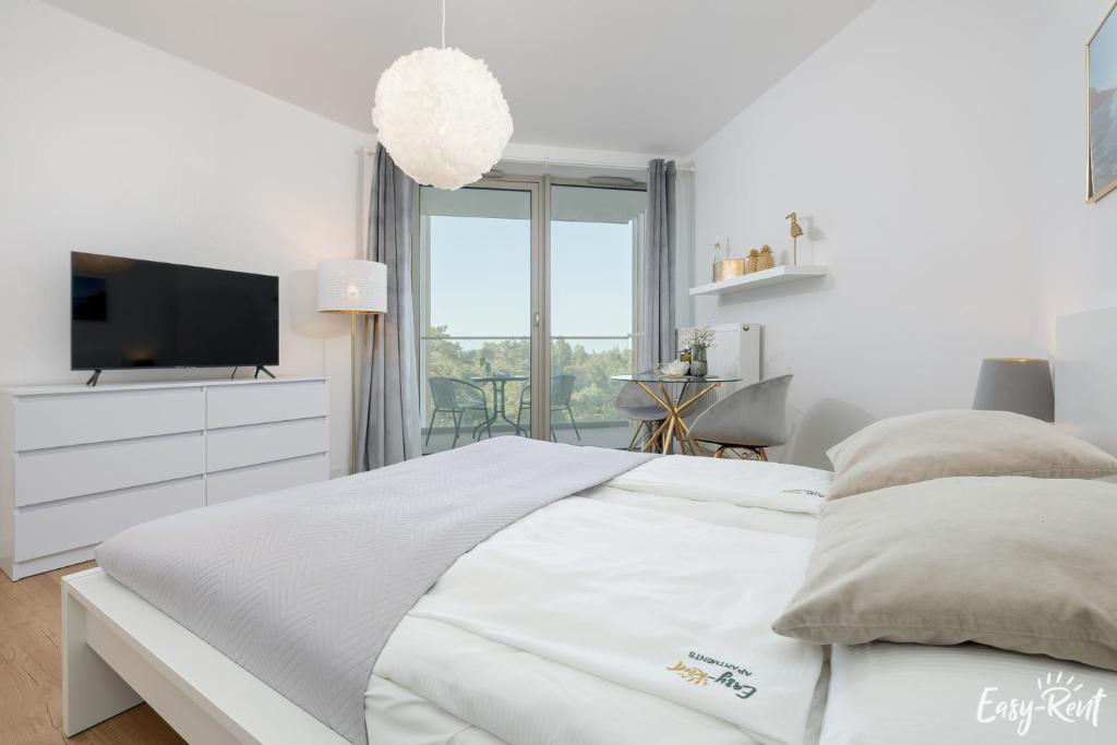 a white bedroom with a bed and a tv at Pinea 620 - Easy - Rent Apartments VI piętro z widokiem na morze in Pobierowo