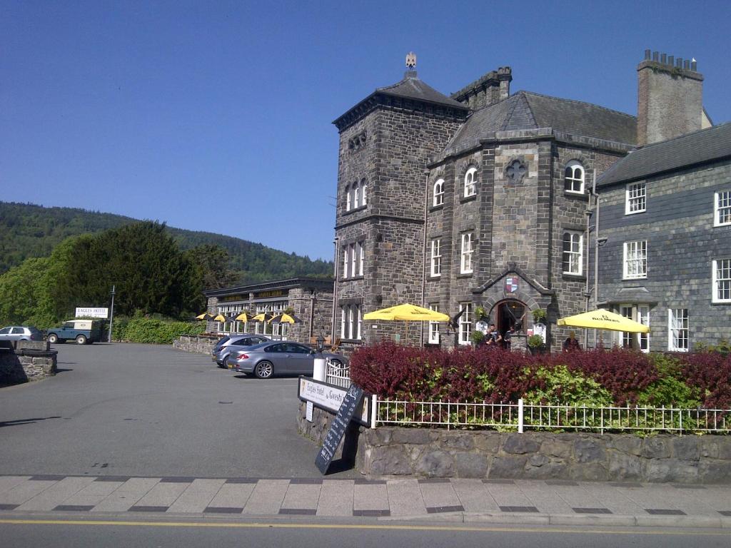 een groot stenen gebouw met gele parasols op een parkeerplaats bij The Eagles Hotel in Llanrwst