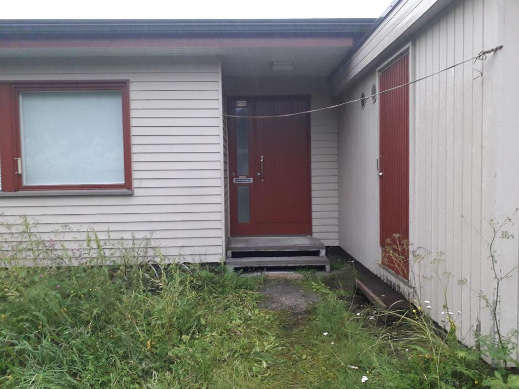 a white house with a red door and some grass at rowhouse for 4 people with 2 rooms in Kemi