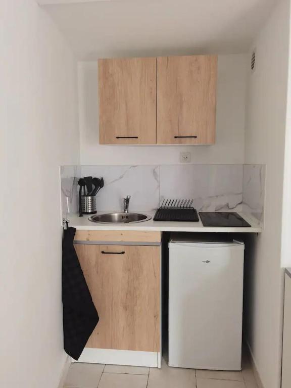 Elle comprend une petite cuisine avec des placards en bois et un évier. dans l'établissement Studio 1 - Métro Europe Rouen, à Rouen