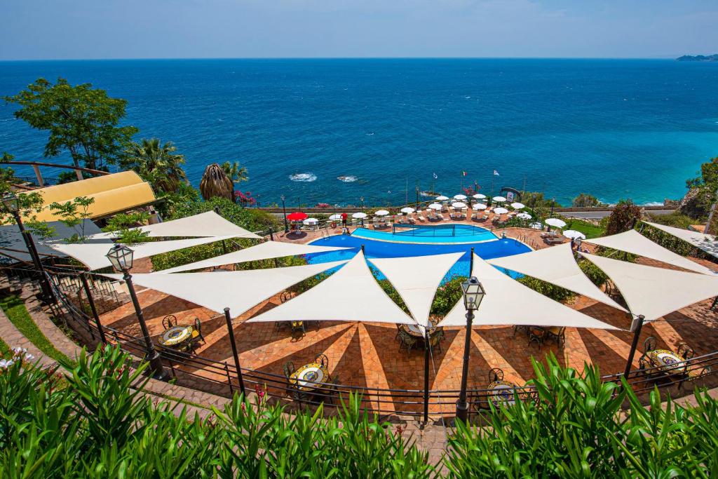 a view of a pool with umbrellas and the ocean at Baia Taormina - CDSHotels in Forza dʼAgro