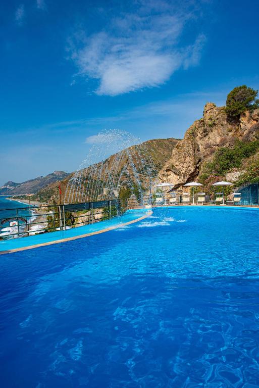 a swimming pool with blue water and a mountain at Baia Taormina - CDSHotels in Forza dʼAgro