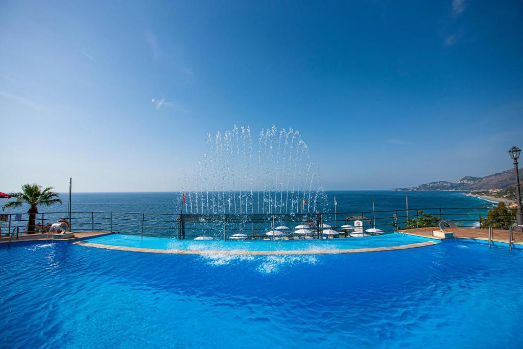 a large swimming pool with a fountain in front of the ocean at Baia Taormina - CDSHotels in Forza dʼAgro