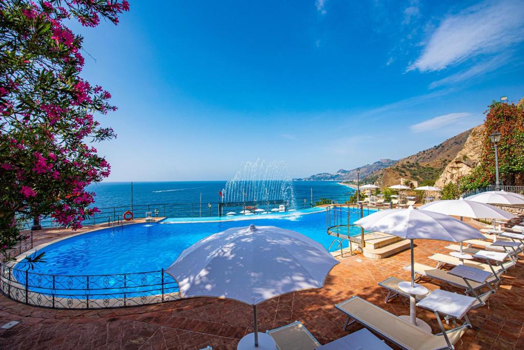 a swimming pool with chairs and umbrellas and the ocean at Baia Taormina - CDSHotels in Forza dʼAgro