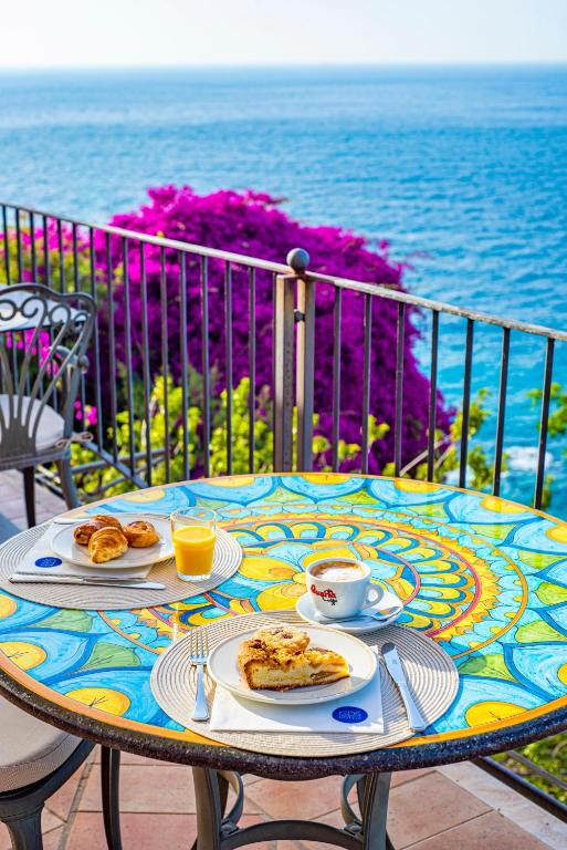 a table with plates of food on a table with the ocean at Baia Taormina - CDSHotels in Forza dʼAgro
