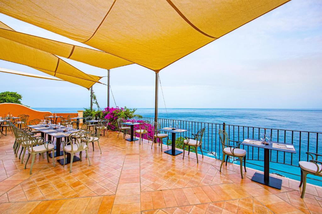 a patio with tables and chairs and the ocean at Baia Taormina - CDSHotels in Forza dʼAgro