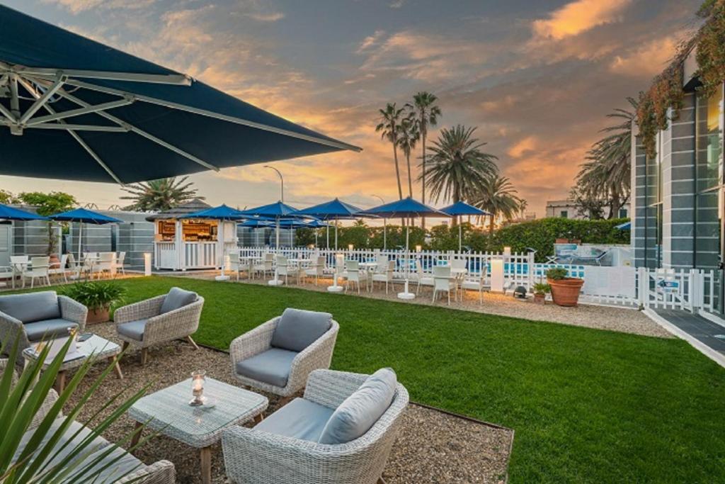 a patio with chairs and tables and blue umbrellas at Hotel Excelsior in Marina di Massa