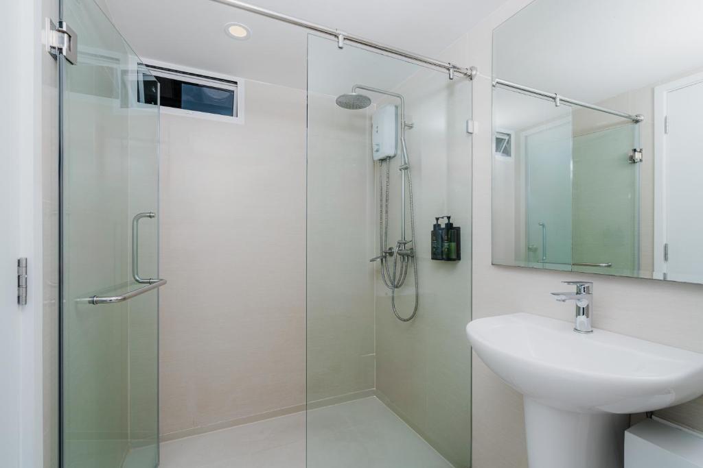 A compact bathroom with a glass-enclosed rainfall shower and pedestal sink.