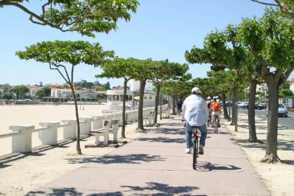 ein Mann, der mit dem Fahrrad einen Bürgersteig mit Bäumen entlang fährt in der Unterkunft plain pied proche de la plage in Saint-Georges-de-Didonne
