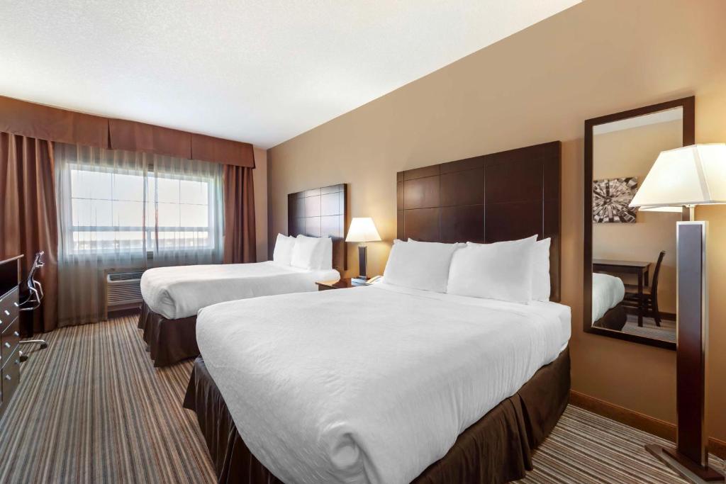 a hotel room with two beds and a mirror at Best Western Plus Peace River Hotel & Suites in Peace River