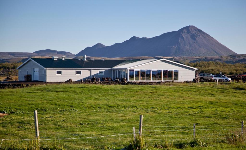 a white barn in a field with a mountain in the background at Vogafjós Farm Resort in Myvatn