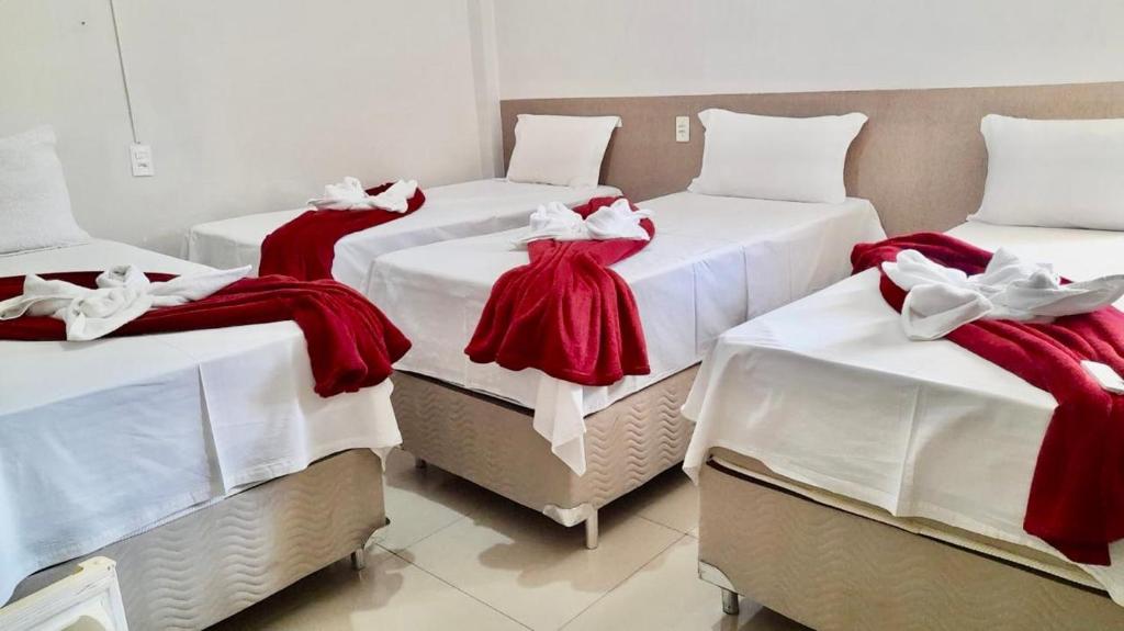 três camas num quarto com cobertores vermelhos e brancos em Hotel Arco Iris Palmas em Palmas