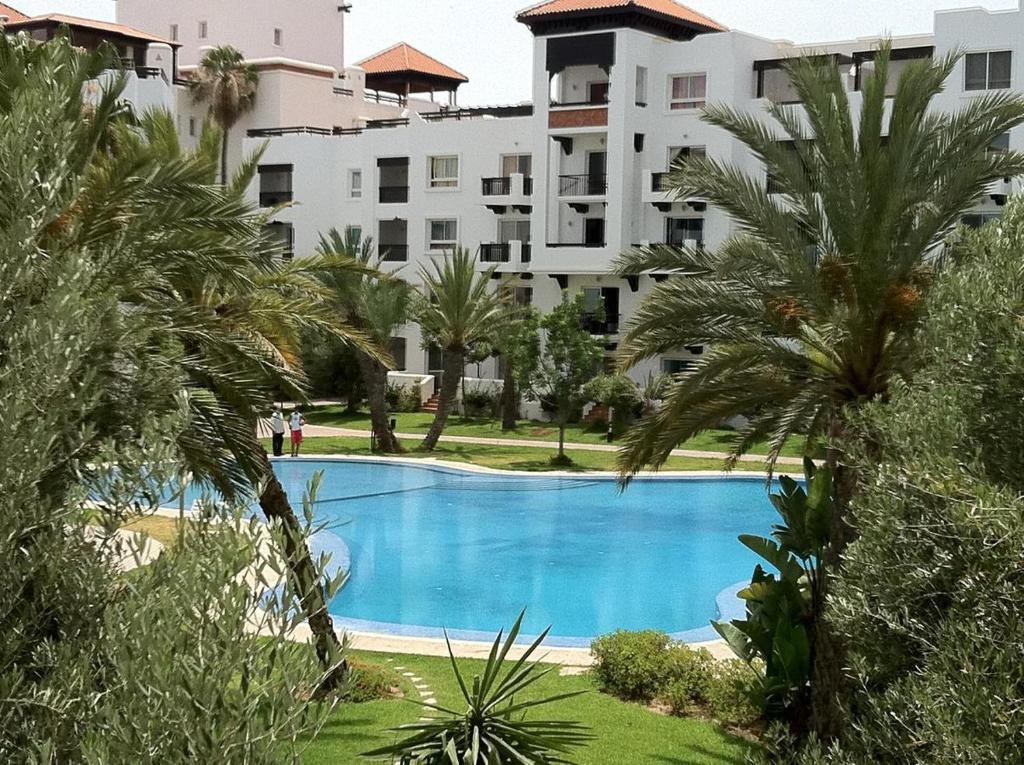 a swimming pool in front of a building with palm trees at AGADIR MARiNA - LUXURY BEACHFRONT APARTMENT in Agadir