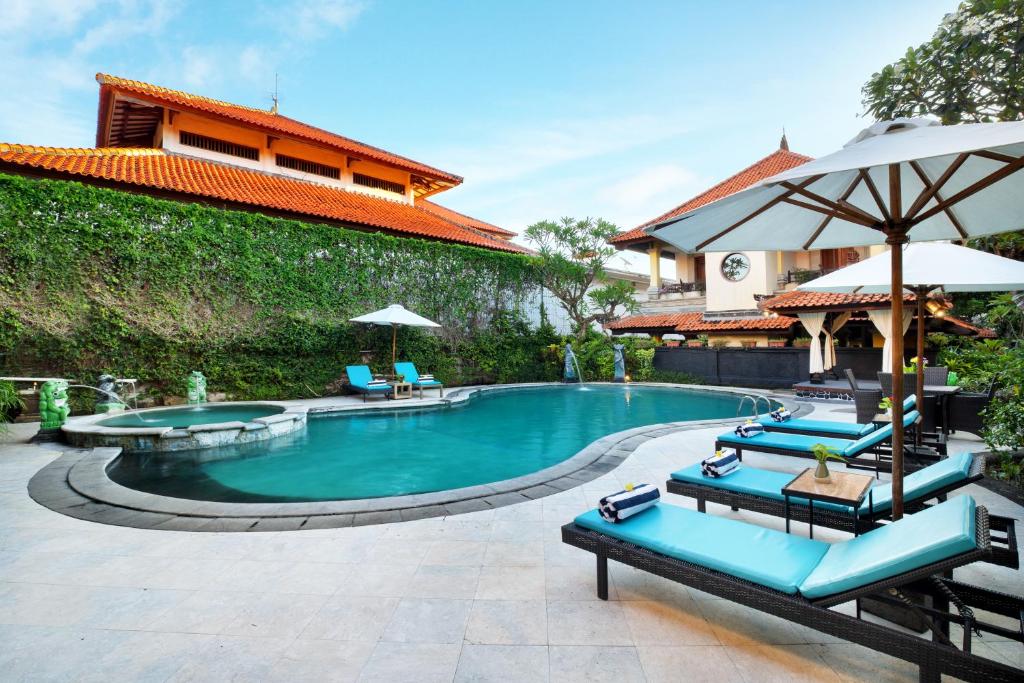 a pool with chairs and umbrellas next to a building at Villa at Royal Tunjung Bali in Seminyak