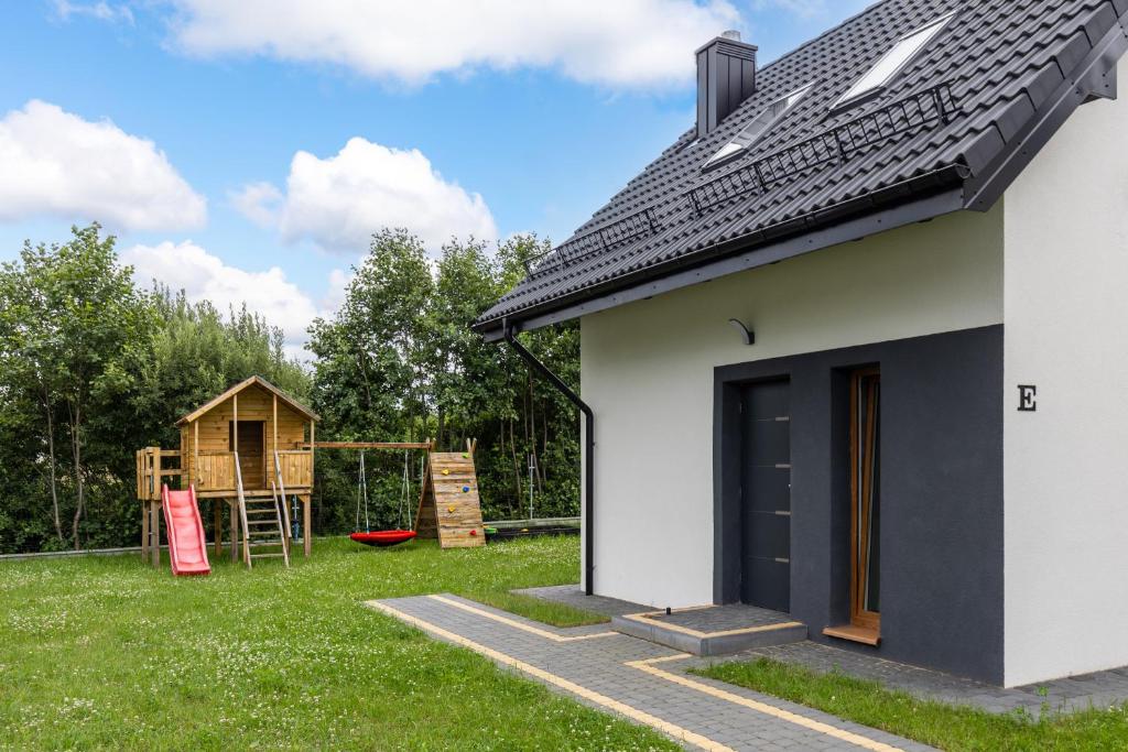a white house with a playground in the yard at Domki Niedźwiadki nad morzem in Kopalino