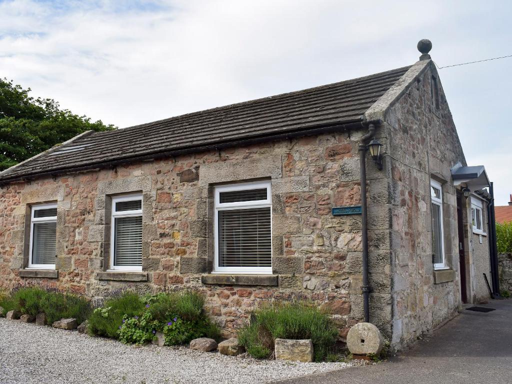 an old stone building with three windows on a street at The Old Reading Room in Bamburgh