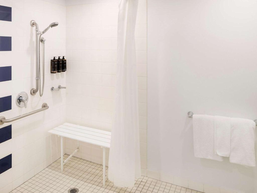 a white bathroom with a shower with a bench at Mercure Melbourne Southbank in Melbourne