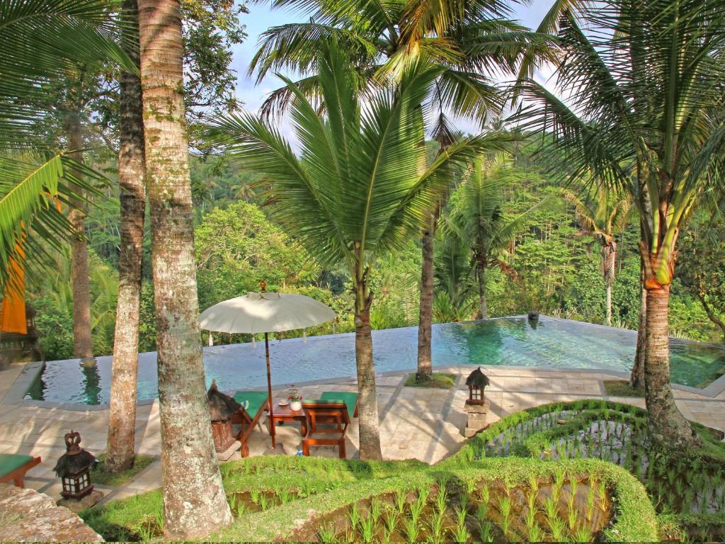 a pool with palm trees and chairs and an umbrella at Toya Retreat Villa in Tegalalang