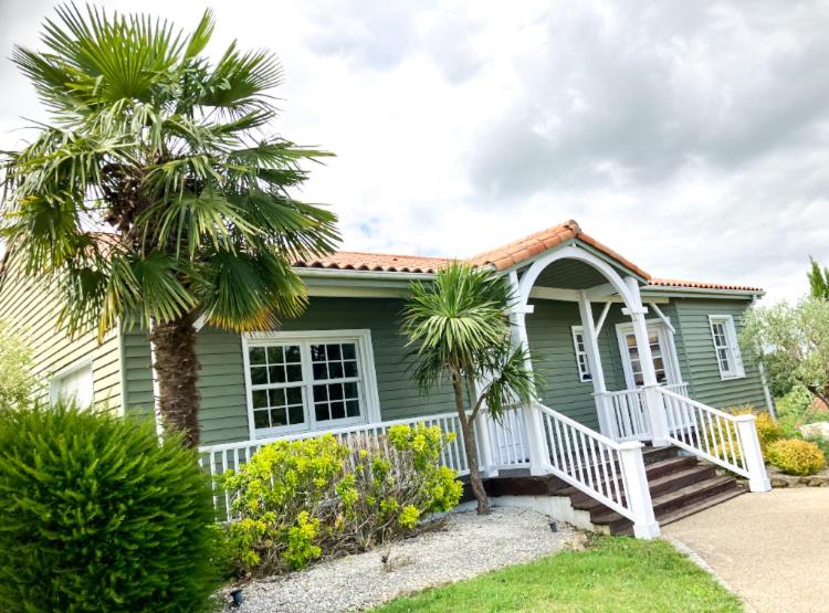 une maison verte avec des palmiers devant elle dans l'établissement Un petit bout de Louisiane chambre d'hôtes avec Piscine et Petit Déjeuner, à Chantonnay