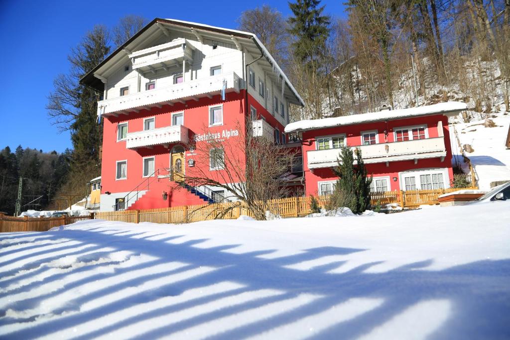 un grand bâtiment rouge avec de la neige au sol dans l'établissement Gästehaus Alpina, à Berchtesgaden