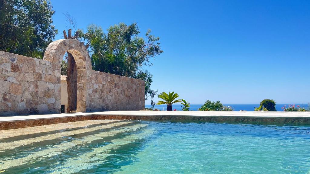 a swimming pool next to a stone wall and the ocean at Auberge Ferayola in Galeria