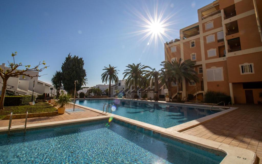 a large swimming pool with palm trees and buildings at Apartamento superior - Alcocebre in Alcossebre