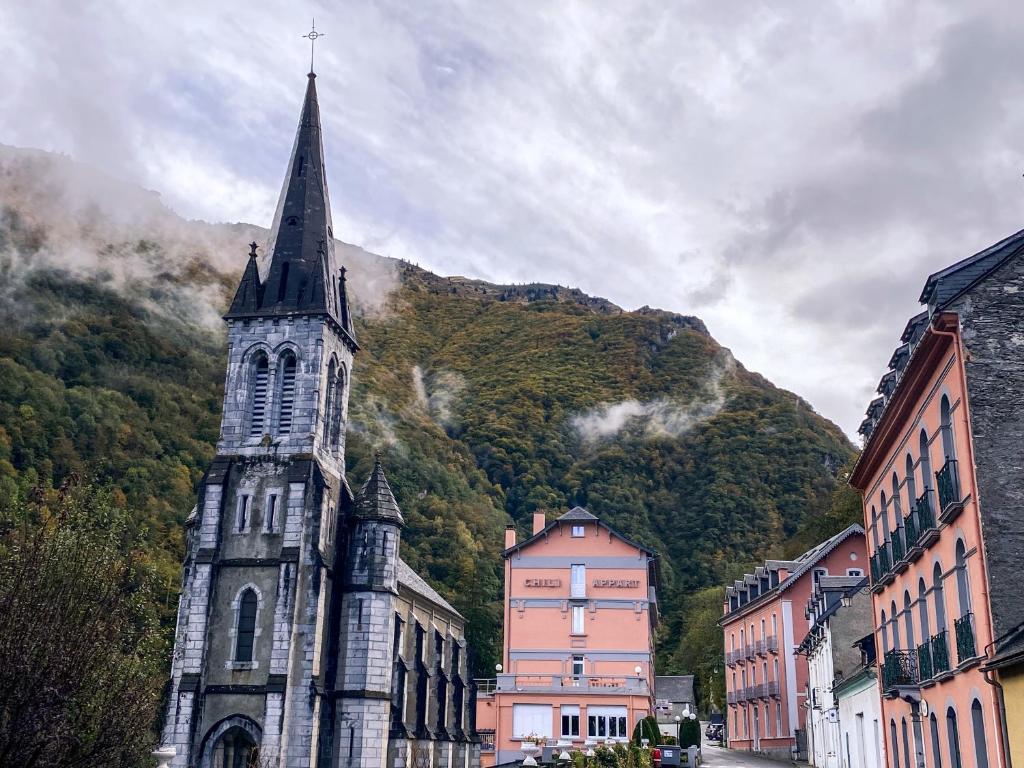 une église avec une cloche en face d'une montagne dans l'établissement Appartement Luz Saint Sauveur / Tourmalet, à Luz-Saint-Sauveur