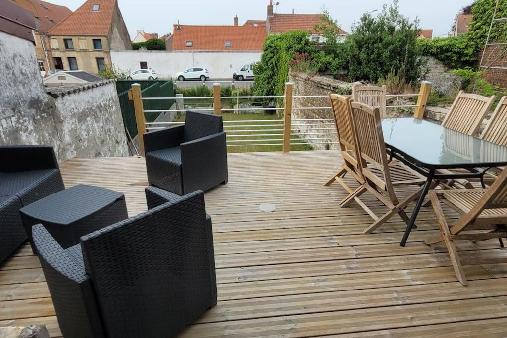 une terrasse en bois avec une table et des chaises en verre dans l'établissement Maison de ville refaite à neuf, à Bourbourg