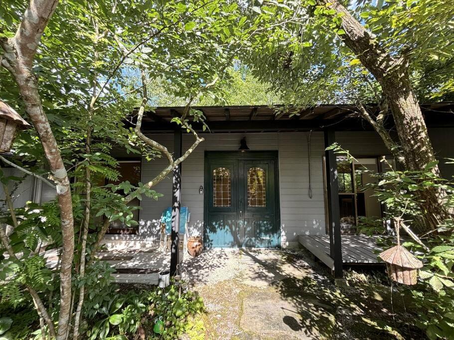 a white house with a green door and trees at sorairo in Kumanoshō