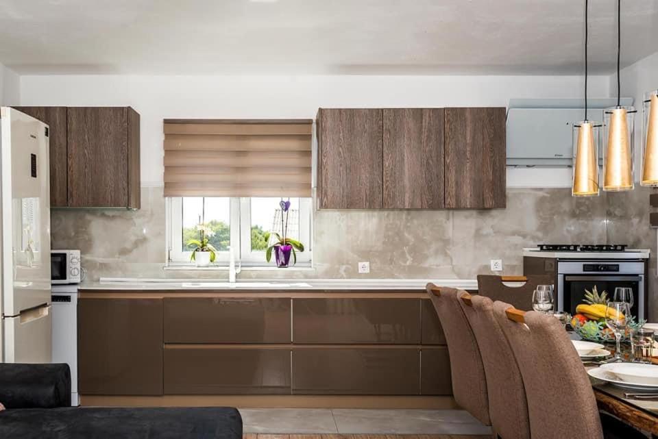 eine Küche mit braunen Schränken, einem Tisch und einem Fenster in der Unterkunft Apartman Brodarica Sibenik in Brodarica