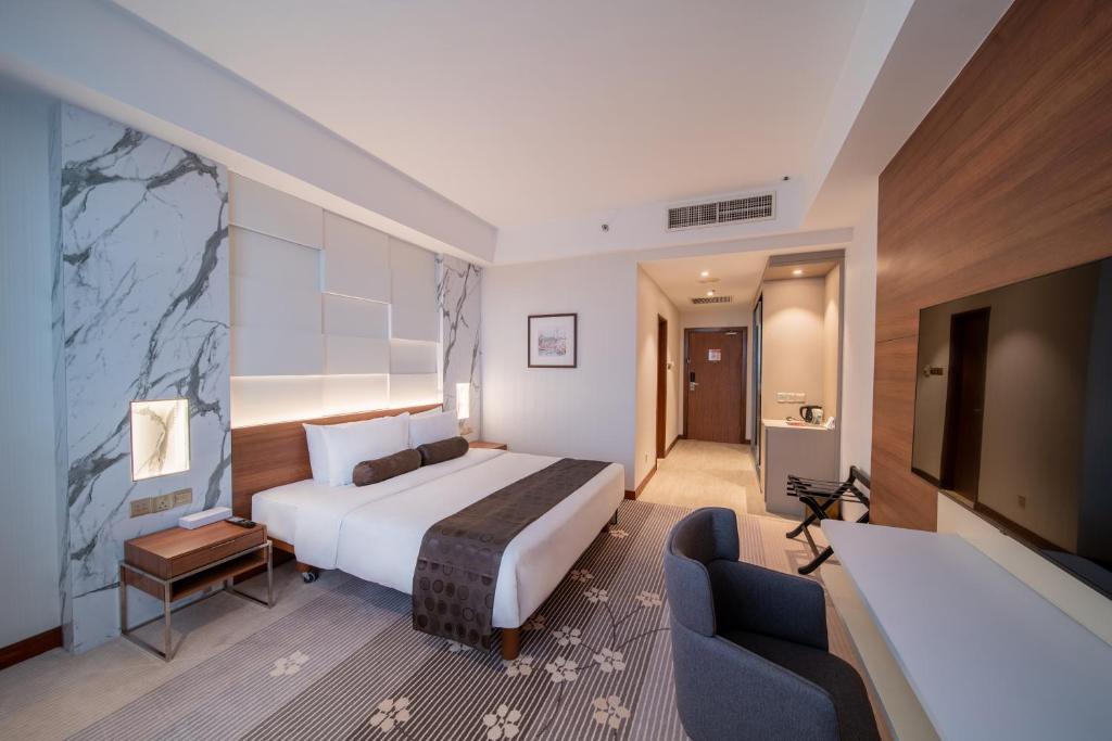 A refined guest room with a large bed, television, lounge chair, and writing desk.