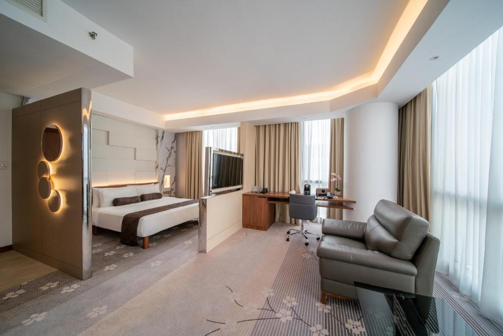 A contemporary room with a bed, sitting chair, desk, and city-facing windows.