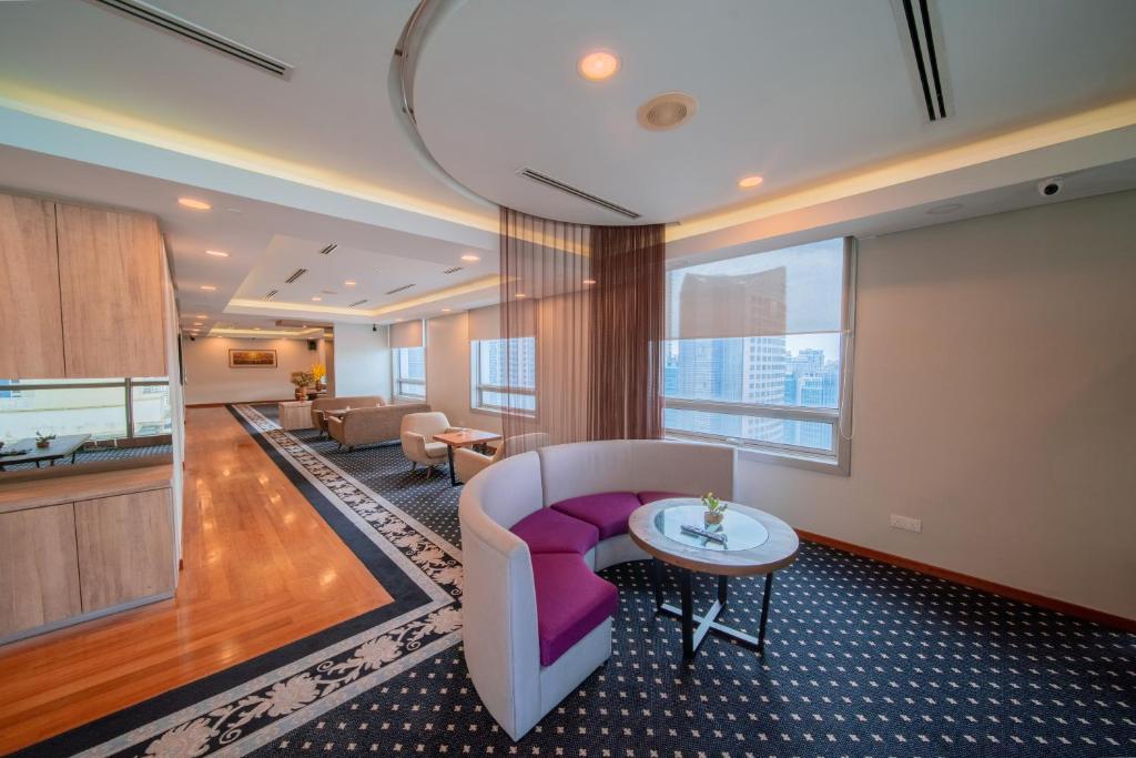 A spacious hotel sitting area with a curved sofa, armchairs, wood flooring and city-facing windows.