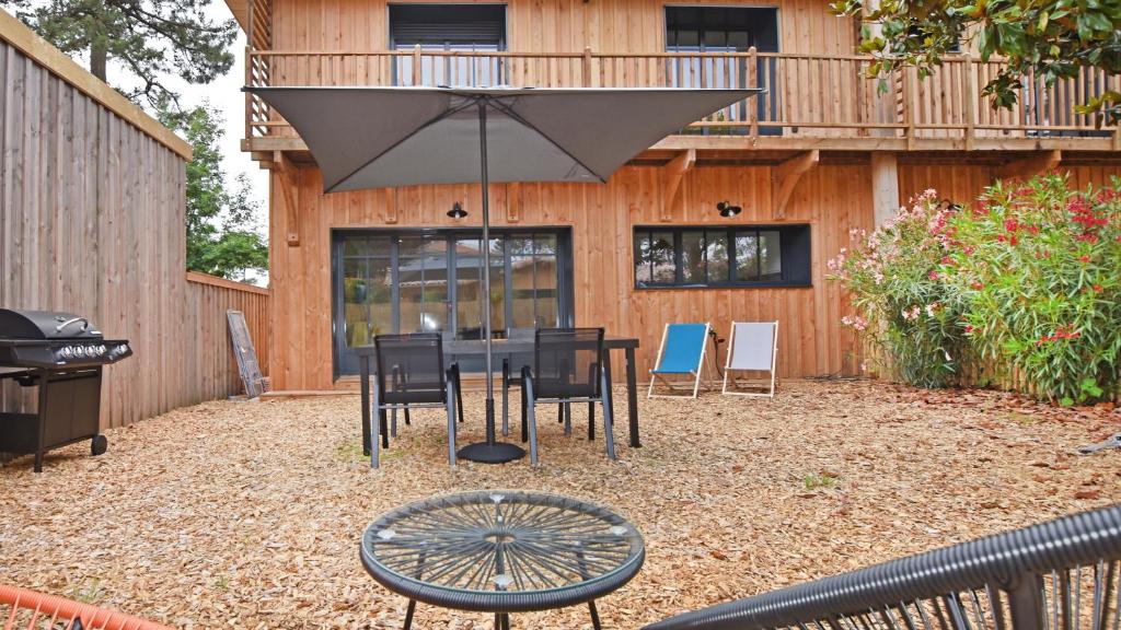 un patio avec une table, des chaises et un parasol dans l'établissement Maison 4 chambres, Petit Piquey, à Lège-Cap-Ferret
