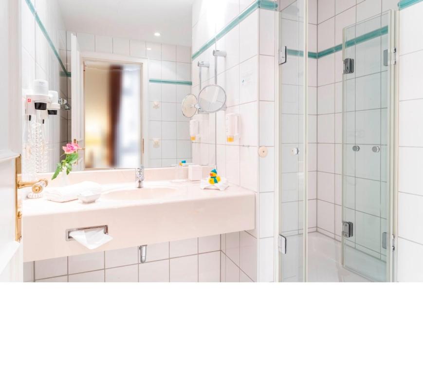 a white bathroom with a sink and a shower at Strandhotel Sylt Westerland in Westerland