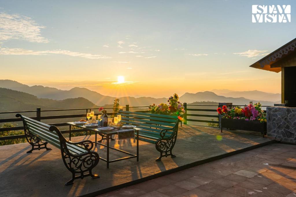 a patio with a table and chairs and the sunset at Chalet Rushli - Free Breakfast with Valley View at Mussoorie by StayVista in Kanatal