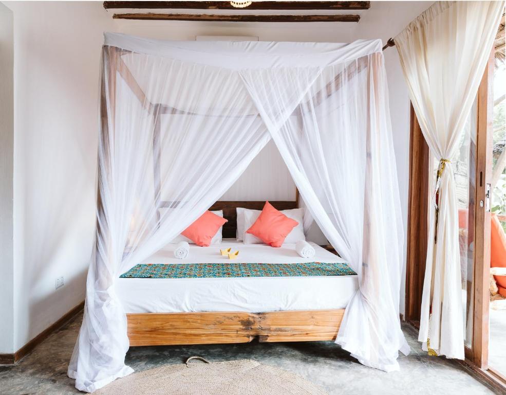 a bedroom with a canopy bed with red pillows at Bahati Sunset Bungalows Michamvi in Michamvi