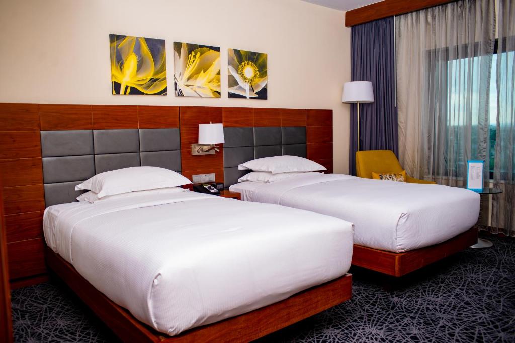 two beds in a hotel room with white sheets at Hilton Garden Inn Nairobi Airport in Nairobi
