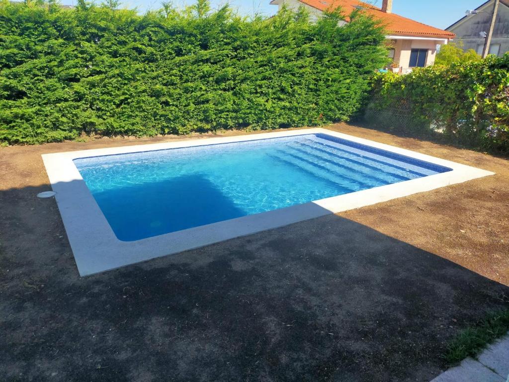 a swimming pool in a yard next to a hedge at Chalet independiente zona Coruxo in Oya