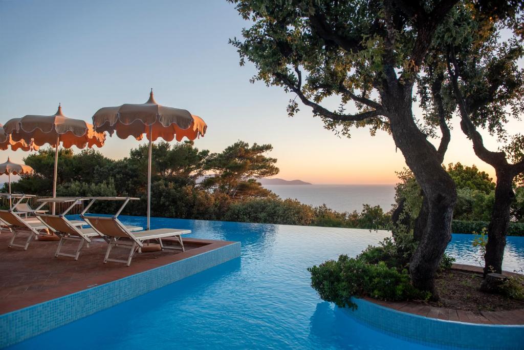 a pool with chairs and umbrellas and the ocean at Boutique Hotel Torre Di Cala Piccola in Porto Santo Stefano