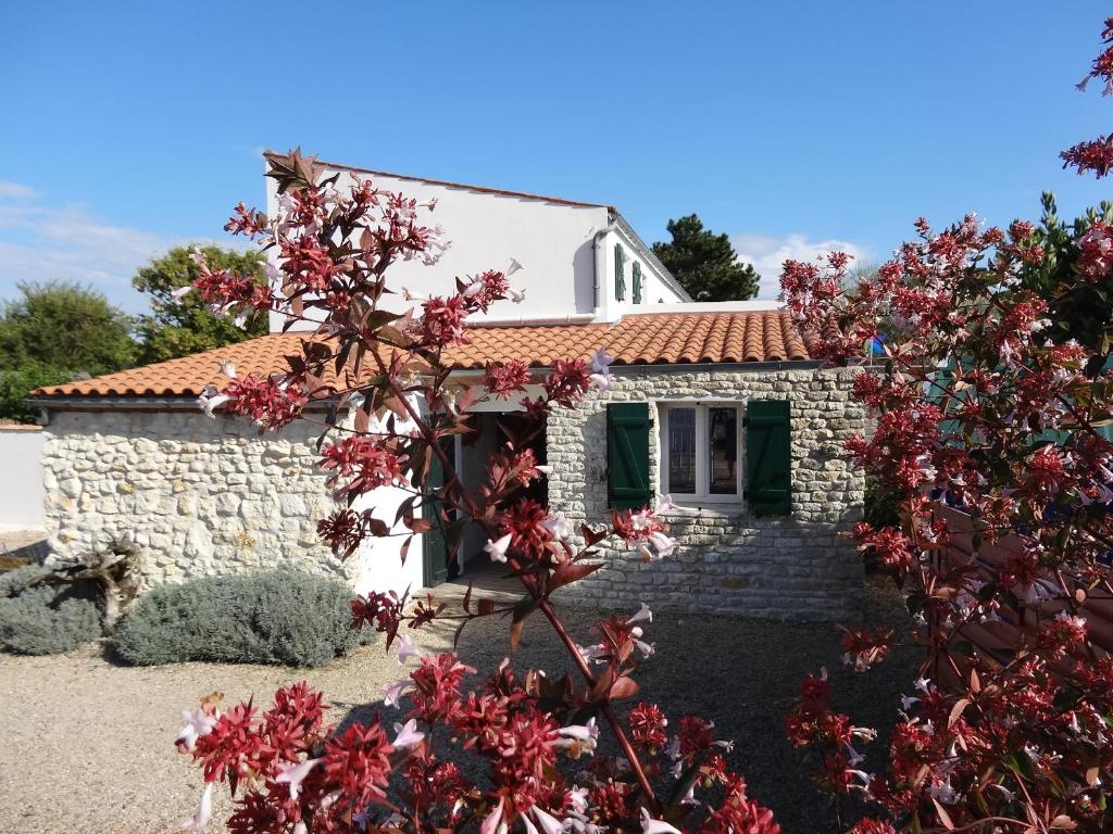 une maison en pierre avec des fleurs rouges devant elle dans l'établissement Séjour en famille à Avail, à Dolus-d'Oléron