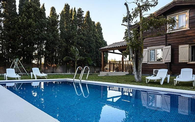 a swimming pool with white chairs and a house at Casa Pinares de Roche tres dormitorios in Cádiz